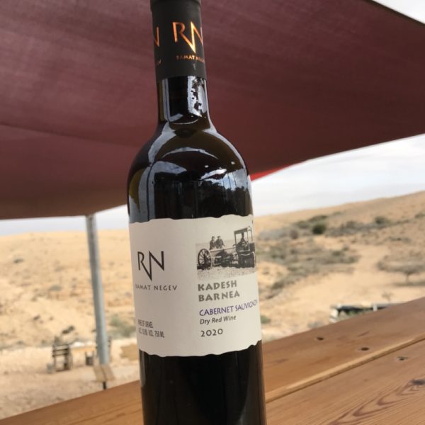 בקבוק יין אדום של יקב רמת נגב, ניצב על בר העץ כשברקע בנוף המדברי המפורסם של חוות קורנמל