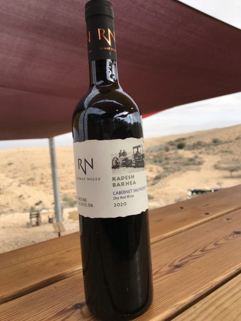 בקבוק יין אדום של יקב רמת נגב, ניצב על בר העץ כשברקע בנוף המדברי המפורסם של חוות קורנמל